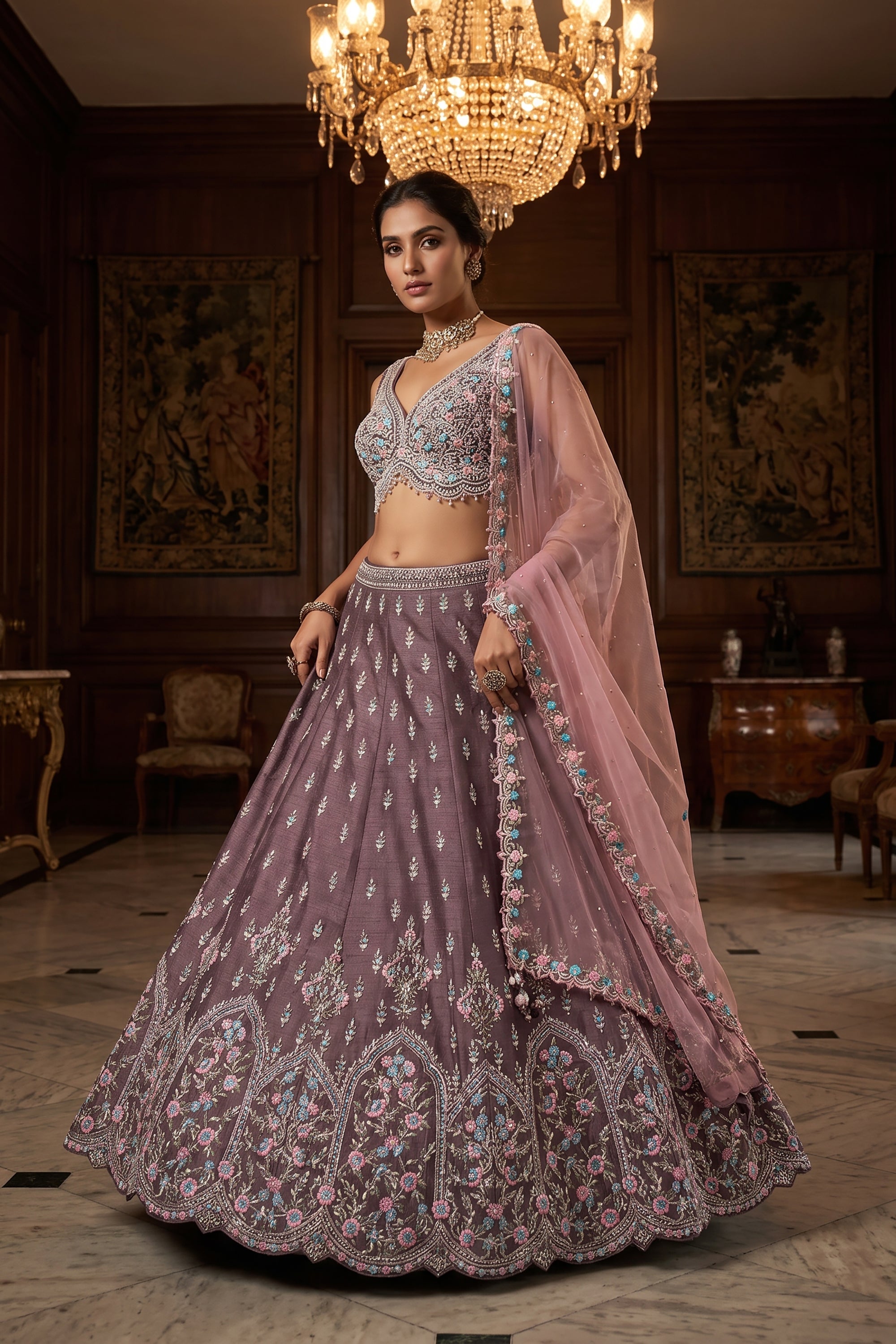 A model wears a mauve raw silk lehenga choli decorated with pastel pink and aqua Resham embroidery, featuring a draped sheer net dupatta in a luxurious mansion setting.