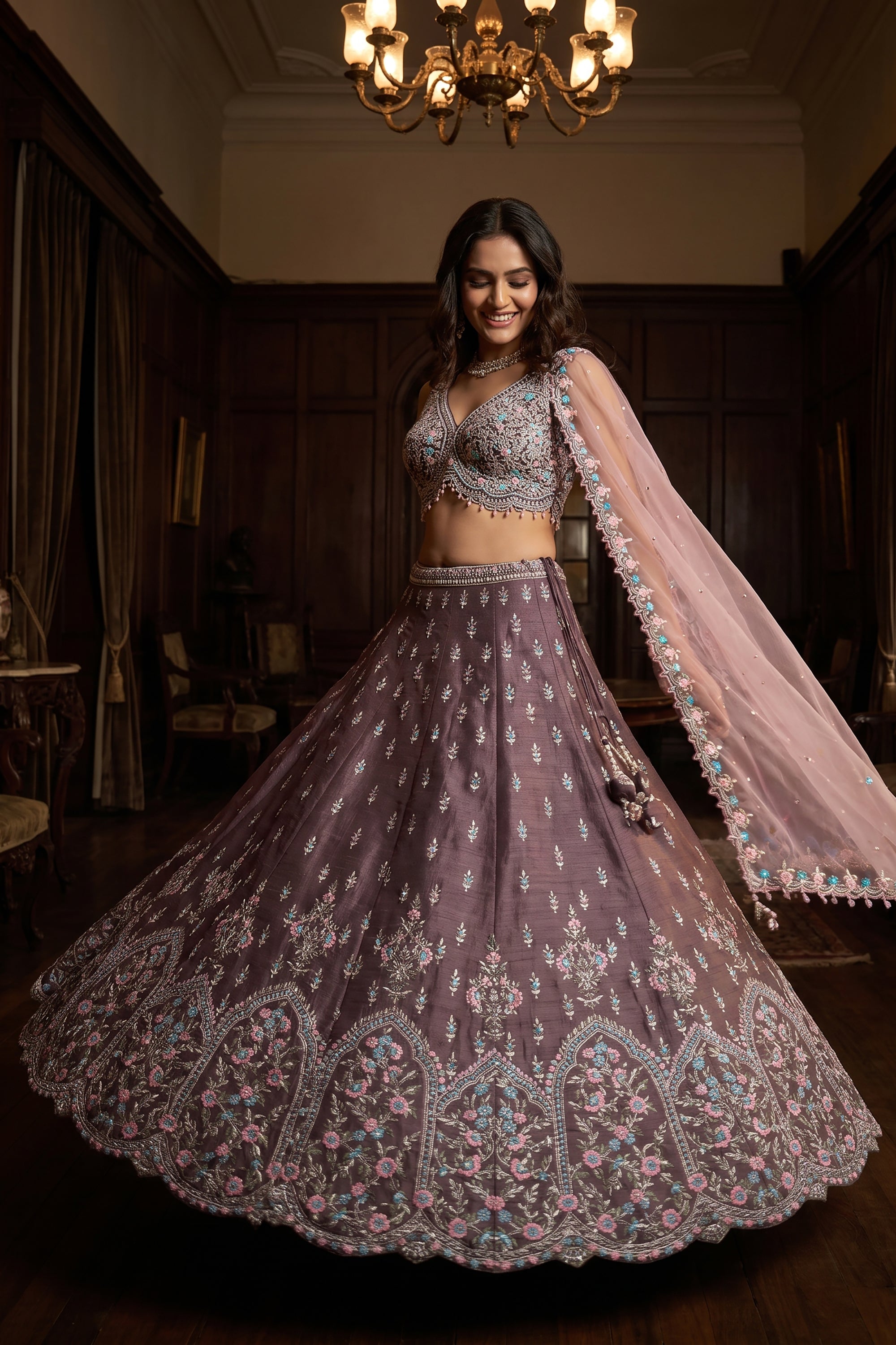 A model wears a mauve raw silk lehenga choli decorated with pastel pink and aqua Resham embroidery, featuring a draped sheer net dupatta in a luxurious mansion setting.